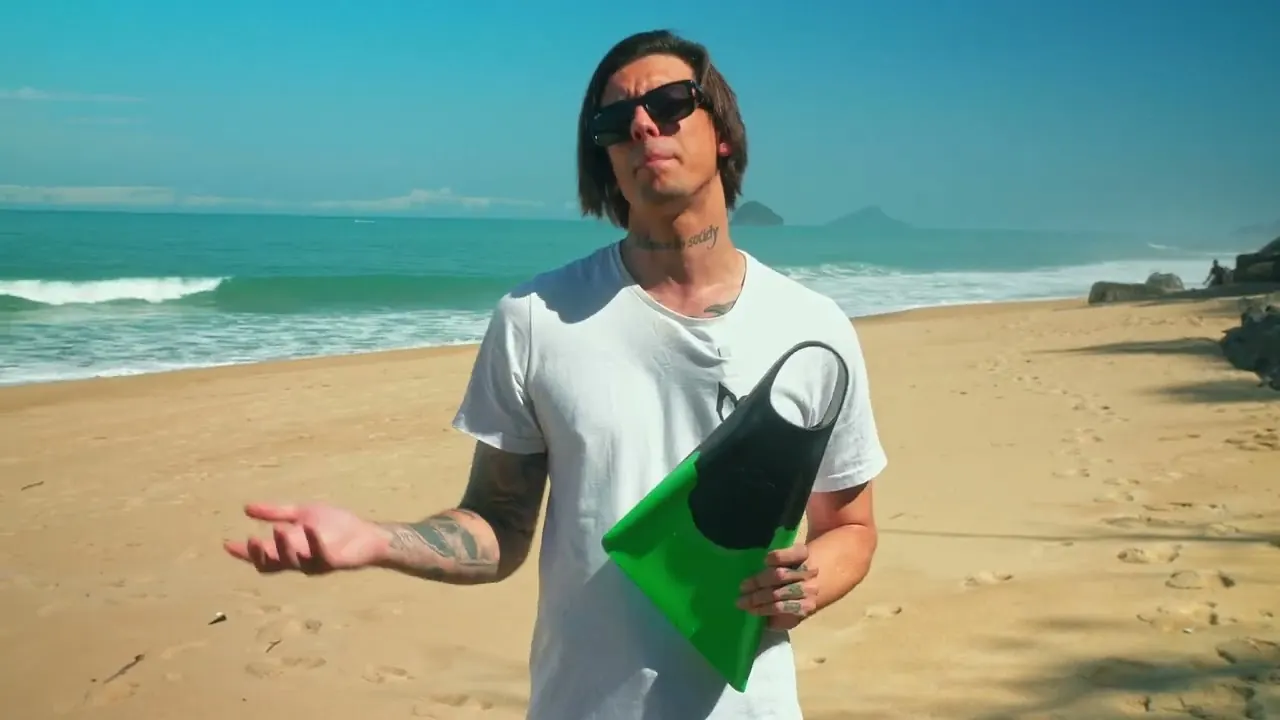 Atleta na praia segurando uma nadadeira Magik verde e preta